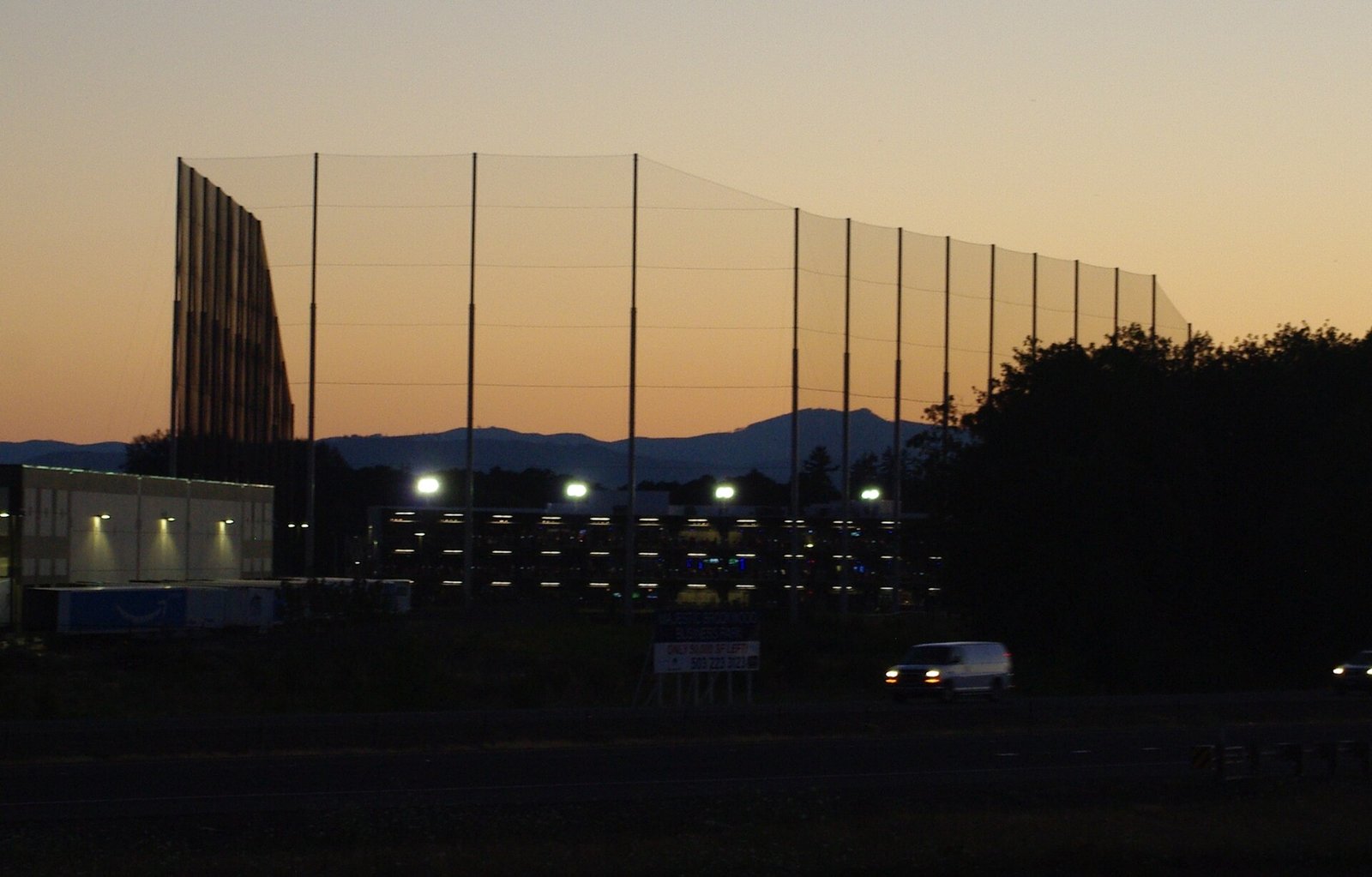 A Topgolf venue at sunset with rows of bays lit for the evening