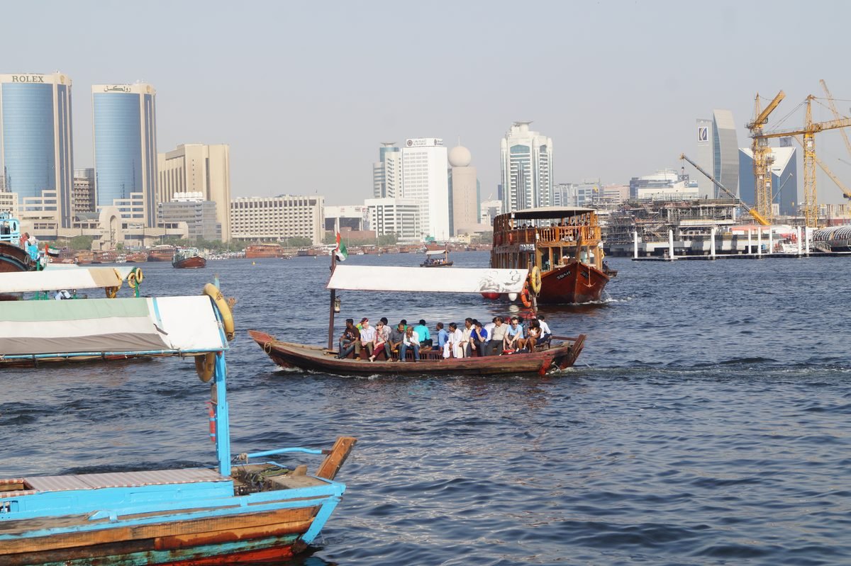 A traditional dhow carrying passengers across Dubai Creek, the old Dubai side of the dhow cruise creek experience