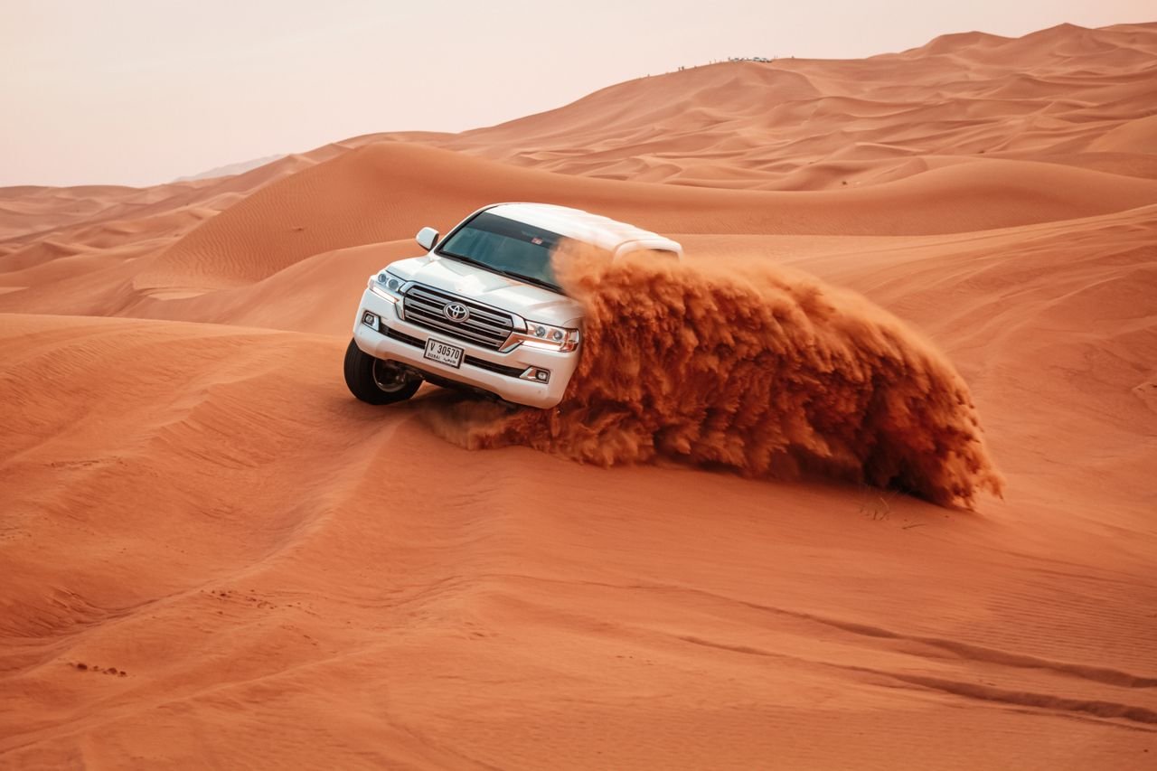 Land Cruiser dune bashing with a wave of sand on a Dubai desert safari
